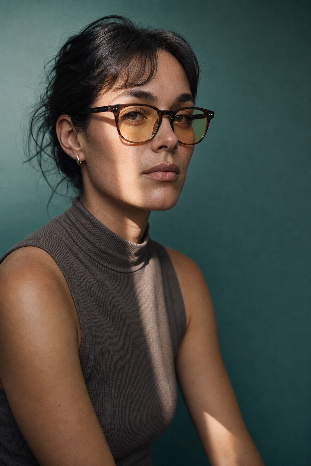 A woman in glasses looking towards the camera against a deep green backdrop